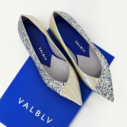 V A L B L V pointed toe ballerina flats in silver glitter and reflective stardust patent leather on a blue shoe box.